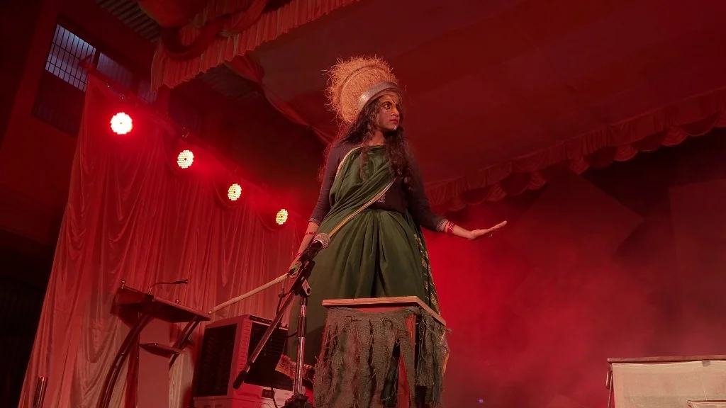 Actor performing intense monologue under dramatic red stage lighting in Mayadveepa