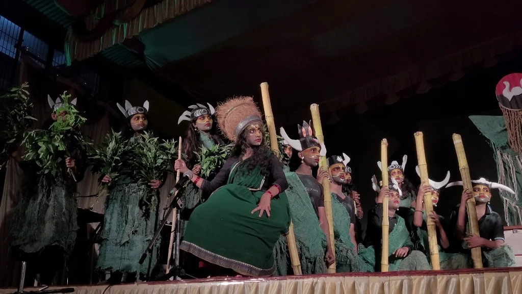 Full 20-student ensemble finale with bamboo spears and foliage in Mayadveepa